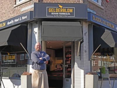 Slagerij Gelderblom met trotse medewerker voor de ingang, omgeven door commerciële teksten en etalageproducten.