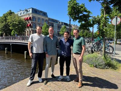 Vier mannen staan samen bij een brug in Haarlem met fietsen en een gebouw op de achtergrond.