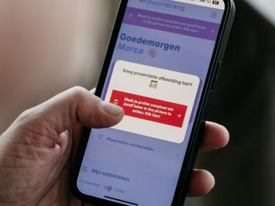 Een hand houdt een smartphone vast met een app-scherm getiteld Goedemorgen Marco, gericht op profielverbetering.