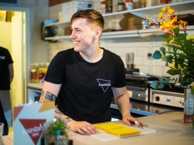 Man in een moderne keuken bereidt een maaltijd voor terwijl hij glimlacht, naast kleurrijke bloemen.