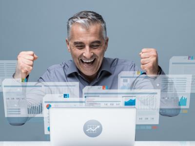 Man juicht achter laptop met grafieken en data, merknaam Valenta linksboven zichtbaar.