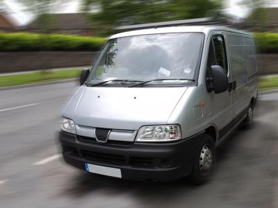 Zilverkleurige bestelwagen rijdend op een weg, geschikt als bedrijfswagen voor koeriers.