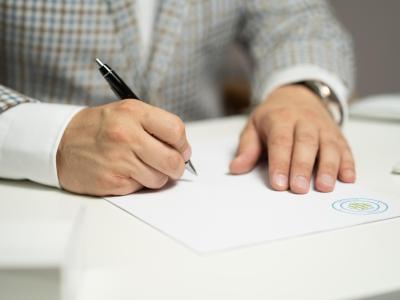 Een man tekent een document aan een bureau met een pen in de hand.