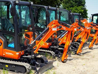 Rij compacte oranje minigraafmachines geparkeerd op een zandterrein.