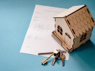 Een houten modelhuisje en sleutels liggen op hypotheekdocumenten tegen een blauwe achtergrond.