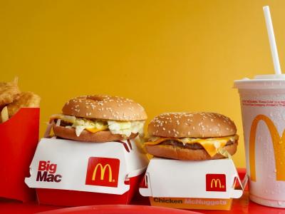 McDonald's maaltijd met frietjes, Big Mac, Chicken McNuggets en een frisdrankbeker tegen een gele achtergrond.