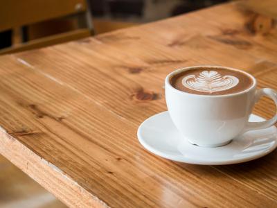 Een cappuccino met latte art op een houten tafel in een gezellige cafésetting.