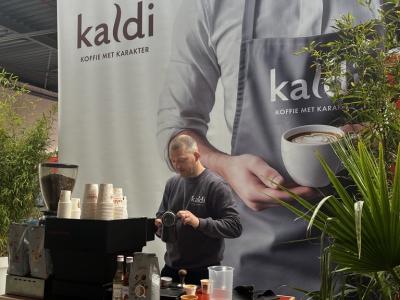 Man bereidt koffie bij een Kaldi-stand met groot spandoek tijdens Franchise+Beurs 2025.