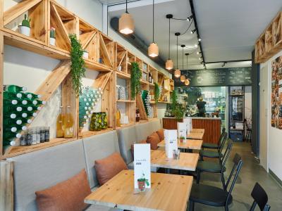 Modern ingericht café met houten meubels, groene accenten en een open keuken in een frisse en eigentijdse stijl.