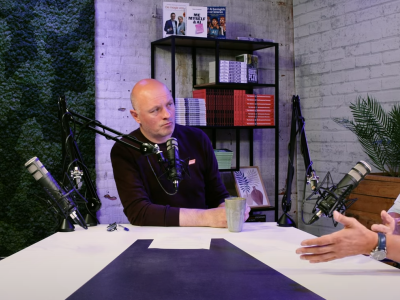 Drie mannen in gesprek tijdens een podcastopname over franchise bij Fortune Coffee, met microfoons en boeken op de achterg...