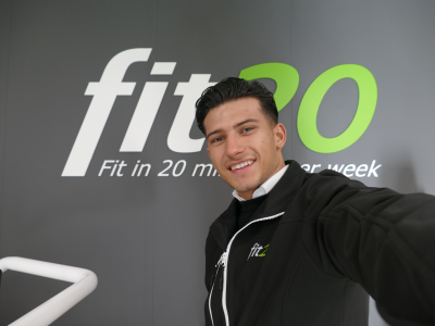 Man in fit20-jack poseert voor fit20-muur met de tekst Fit in 20 minuten per week.