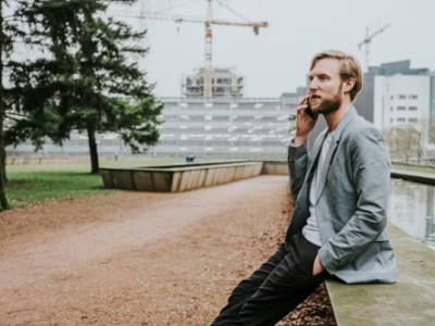 Verkoper in gesprek via mobiele telefoon bij moderne stadsomgeving met bouwkranen op de achtergrond.