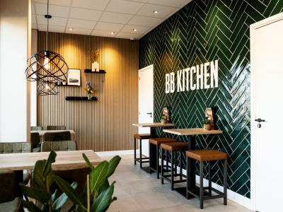 Interieur van BB Kitchen met groene betegelde muur en tafels met hoge stoelen.