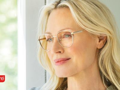 Blonde vrouw met bril staat bij raam, kijkt naar buiten met Eyelove-logo links onderin de afbeelding.
