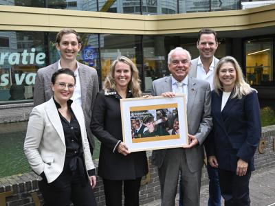 Zes mensen poseren buiten met een ingelijst exemplaar van het McDonald's Nederland Impact Rapport 2024-2025.