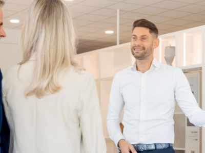 Medewerker in een showroom toont sanitairproducten aan twee klanten onder een verlichte wand.
