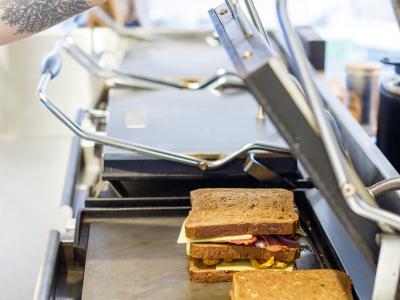 Een tosti-ijzer wordt gebruikt om sandwiches te bereiden, met de handgreep vastgepakt door een persoon.