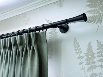 Groene gordijnen hangen aan een zwarte gordijnroede tegen een muur met varenmotief.