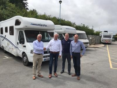 Vier mannen staan voor geparkeerde campers op een verharde oprit, bij een camperdealerschap.