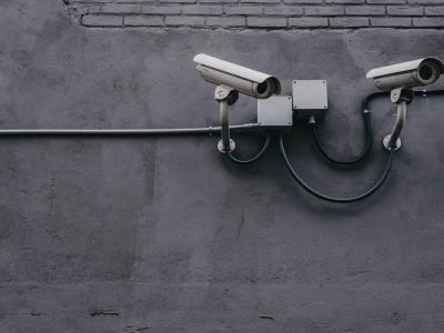Twee beveiligingscamera's gemonteerd op een betonnen muur met bekabeling zichtbaar.