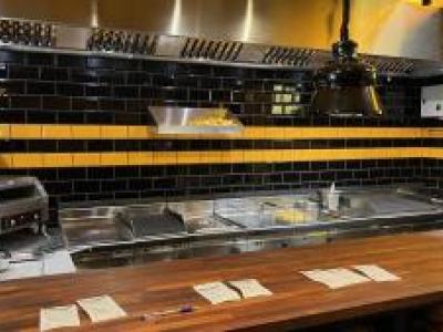 Roestvrijstalen keuken met frituurstation en zwarte tegelmuur in een moderne cafetaria.