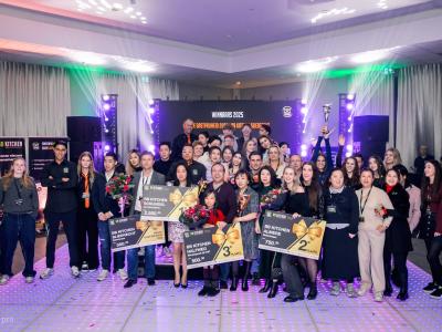 Groepsfoto van winnaars tijdens BB Kitchen Franchisedag 2025 met cheques en bloemen op het podium.