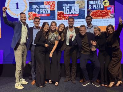 Een groep mensen viert feest op een podium voor een scherm met promoties van New York Pizza.