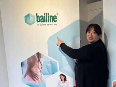 Een vrouw wijst naar een Bailine-poster met het logo en afbeeldingen van ontspanning en massage.