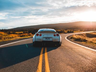 Sportauto rijdt op bochtige weg bij zonsondergang met open landschap op de achtergrond.