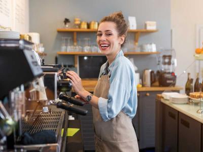 Jonge barista in een moderne koffiebar lacht terwijl ze achter de espressomachine werkt.