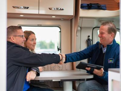 Twee personen schudden handen met een verkoper in een camper terwijl ze een zakelijke transactie bespreken.