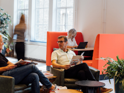 Mensen werken en vergaderen in een modern kantoor met zitruimtes en staantafels, bevorderend voor samenwerking.