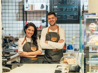 Twee glimlachende barista's in een moderne koffiebar met gebak en drankjes op de toonbank.