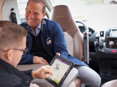 Twee mannen in een camper, een wijst glimlachend naar een tablet waarop getekend wordt.