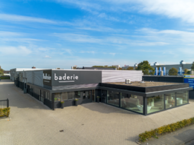 Buitenaanzicht van een modern Baderie gebouw met glazen ramen en Baderie-logo, omgeven door een parkeerterrein.