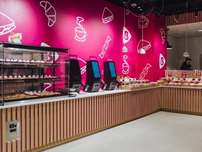 Binnenkant van de Bakker Bart To Go op Utrecht Centraal met felroze wanden, vitrines en scanapparaten.