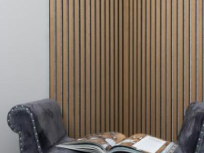 Grijze gestoffeerde stoel met open tijdschrift ervoor een houten lamellenwand.
