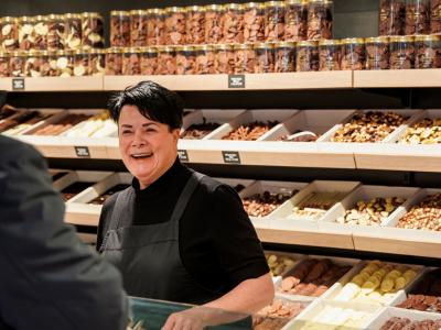 Winkelmedewerker helpt klant bij een wand vol snoep en chocolade in een speciaalzaak.