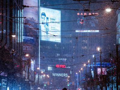 Winternacht in een drukke stad met opvallende verlichte billboards en besneeuwde straten.