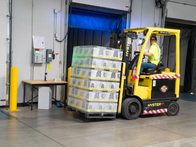 Heftruck met dozen op pallets in magazijnomgeving met open laadruimte.