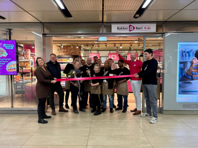 Opening van Bakker Bart To Go pop-up met medewerkers die een lint doorknippen voor de ingang op een station.