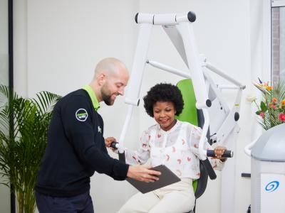 Trainer begeleidt vrouw op trainingsapparaat bij fit20 franchise-vestiging.