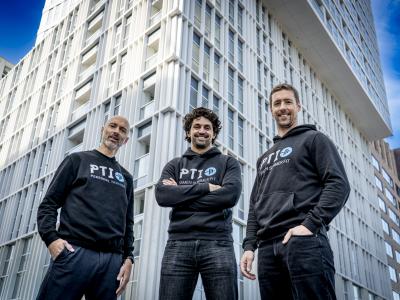 Drie mannen in PTI-hoodies poseren voor een modern kantoorgebouw.