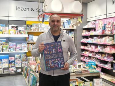 Man in Bruna-winkel houdt een boek vast onder een groot Nijntje-beeld met kleurrijke tijdschriften op de achtergrond.