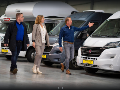 Drie mensen bezichtigen campers in een showroom van Motorhome Depot.