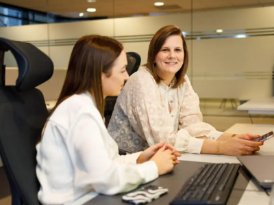 Twee vrouwen in een kantoor bespreken strategie met een laptop en smartphone op een bureau.