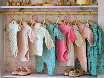 Een rek met kleurrijke babykleding en schoentjes in een kinderkameromgeving.