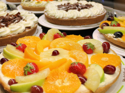 Verschillende kleurrijke vlaaien, versierd met vers fruit en slagroom, uitgestald op een tafel.