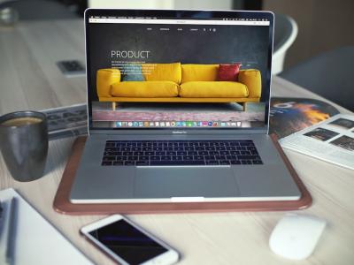 Een opengeklapte laptop met een website op het scherm, omringd door een koffiemok, tijdschrift en smartphone op een bureau.