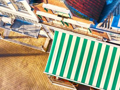 Luchtfoto van een terras met groen-wit gestreepte luifel naast een gebouw met dakramen en terrasstoelen op een zonnige dag.